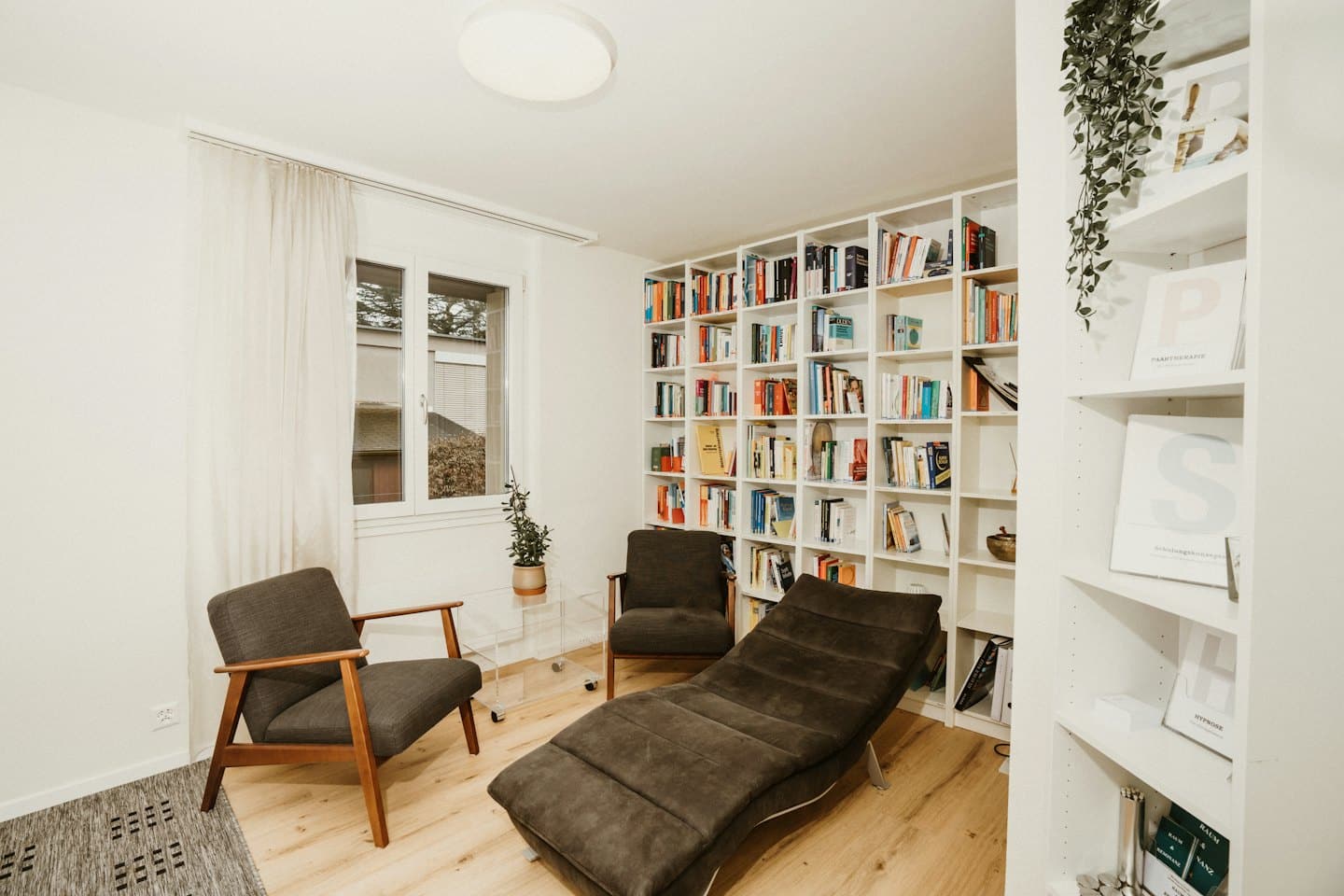 Bureau de thérapeute confortable avec fauteuils, chaise longue et étagères.