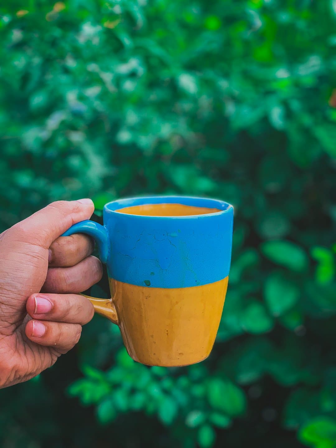 Une main tient une tasse bleue et jaune remplie de café.
